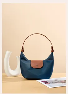 Blue nylon dumpling shoulder bag detail view with brown leather handle and flap closure.