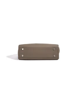 Détail du fond de sac à main en cuir avec quatre pieds métalliques et texture fine.