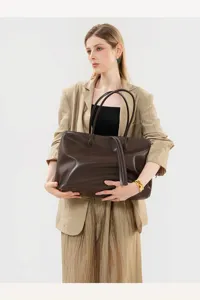 Detailed view of a vintage brown leather tote bag held by a model, showing fine texture.