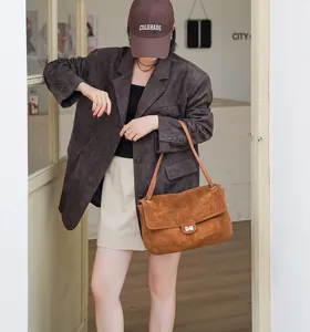 Detailaufnahme der braunen Wildleder-Umhängetasche, getragen von Model im Innenbereich.
