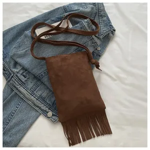 Detalle cercano de un bolso bandolera marrón con flecos para teléfono sobre tela vaquera.