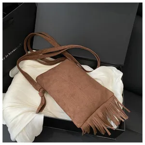 Detalle de bolso cruzado con flecos boho en ante marrón con borlas elegantes en caja de regalo.