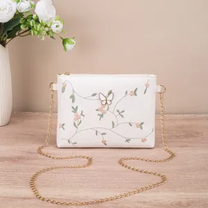 Detailed shot of white embroidered shoulder bag with butterfly accent and gold chain strap.