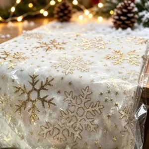 Vista detallada de tela de malla blanca con patrón de copos de nieve dorados para decoración.