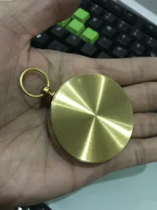 Solid brass pocket compass detail shot, showing vintage circular metal texture and top loop.