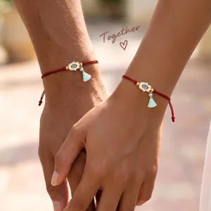 Vista detallada de pulsera roja trenzada unisex con amuleto de mal de ojo y borla.