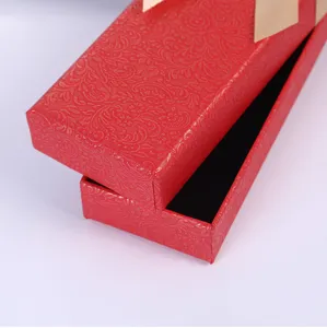 Detalle caja de regalo boligrafo rojo con patron damasco dorado y elegante embalaje de lazo.