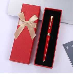 Detalle de caja de regalo roja con lazo dorado y elegante pluma estilográfica.