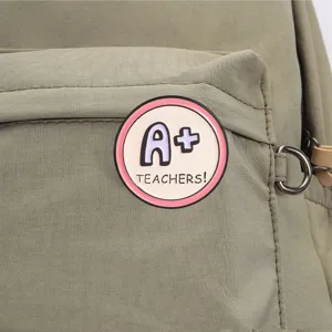 Detailed close-up shot of a cute teacher themed metal brooch badge attached on green backpack fabric.