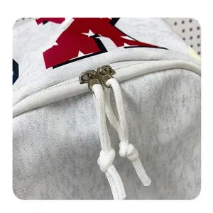 Grauer Rucksack Detailansicht mit doppelten Reißverschlüssen und weißen geknoteten Kordeln.