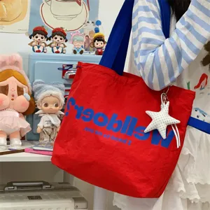 Detail shot of the red canvas tote bag with blue strap and bold letter print and star pendant.