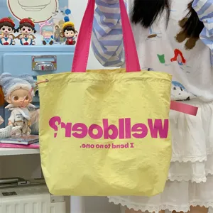 Detailed shot of yellow canvas tote bag with pink straps and letter print for daily use.