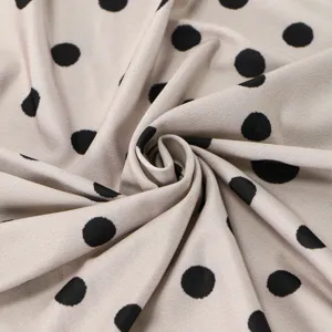 Close-up of soft beige fabric with classic black polka dots, detailed texture view of scarf material.