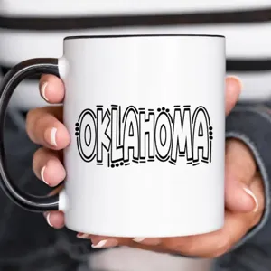 Ceramic coffee mug detail, white cup with black handle and Oklahoma text, office drinkware.
