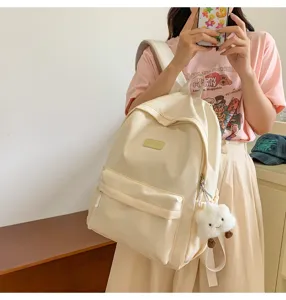 Beige minimalist canvas backpack detail showing front zipper pocket and cute cloud plush pendant.