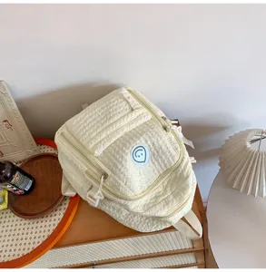 Detail shot of a cute pleated cream backpack with a smiley face patch on a wooden table.