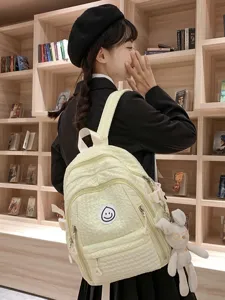 Cute light yellow backpack for women with smiley badge and bunny pendant, sweet casual school bag.