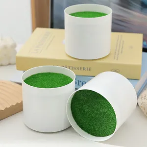 Detailed view of white cylindrical pots filled with green artificial moss on a decorated desk.