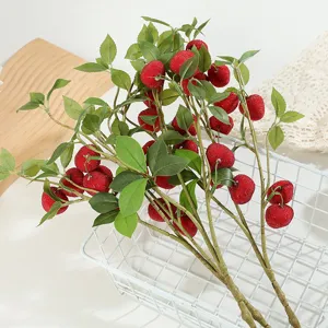 Dettaglio ramo di bacche rosse artificiali, frutta floccata e foglie verdi per arredo.