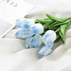Detailed view of artificial blue gradient tulip bouquet with green leaves on white cloth.