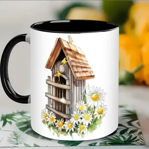 Weißer Keramik-Kaffebecher mit Aquarell-Vogelhaus- und Gänseblümchen-Muster und schwarzem Henkel.
