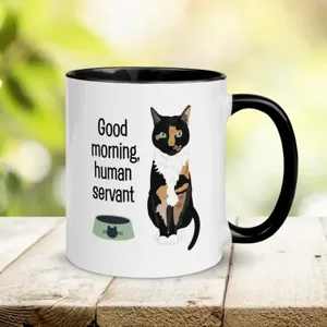 Nahaufnahme einer weißen Keramiktasse mit schwarzem Henkel und süßem Katzenmotiv.