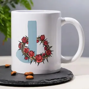 Close-up detail of white ceramic coffee mug featuring custom letter J and thorn rose graphic print.