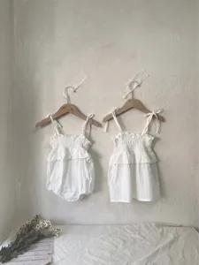 Details van de witte katoenen babymeisje jurk en romper met gesmokte volants en bandjes.