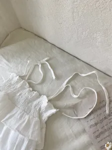 Detail van de witte katoenen zomer jurk voor baby's met fijne jacquard textuur en schattige volants.