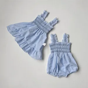 Blue checkered baby girl smocked strap dress detail, summer sleeveless toddler outfit close-up.