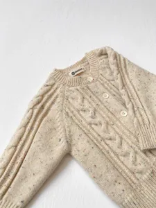 Dettaglio cardigan in maglia per neonati con macchie colorate, lana morbida e trecce.
