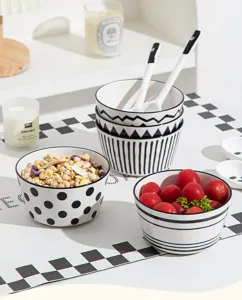 Gros plan de bols en céramique noire et blanche à motifs, remplis de céréales et tomates.
