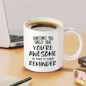 Detailansicht einer weissen Keramiktasse mit inspirierendem Text fuer das Buero auf dem Tisch.