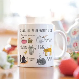 Vista detallada de una taza de cerámica blanca con divertido diseño de gato y texto.