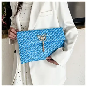 Elegante bolso de mano azul tejido con mariposa dorada y detalle de borla muy chic.