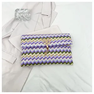 Primer plano del detalle del bolso de mano tejido con patrón de cheurón y borla de mariposa dorada.