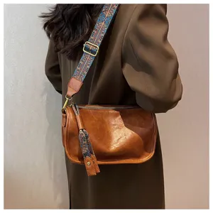 Close-up detail of soft leather crossbody pillow bag with wide ethnic patterned strap.