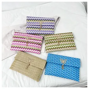 Detalle de bolso clutch de paja tejida, con dije de mariposa de metal y borla, varios.
