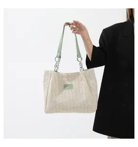 Detail view of woven straw shoulder tote bag with chain straps and green leather handles.
