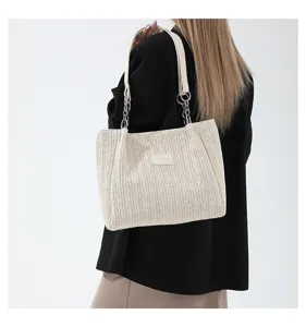 Woven straw shoulder bag detail shot, beige summer beach tote with chain strap and patch.