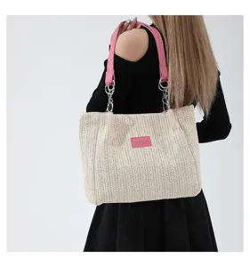 Detailed view of summer straw woven shoulder bag with pink leather strap and metal chain.