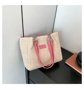 Detail shot of the woven straw tote bag featuring pink leather straps and metal chain links.