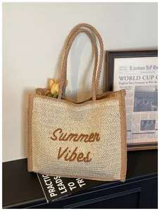 Close-up detail of the straw tote bag showcasing the stylish brown embroidered text detail.