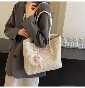 Chic straw woven tote bag detail showing contrast color shoulder straps and cute plush charm.