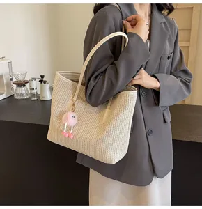 Detail shot of women's straw woven tote bag with shoulder strap and cute fluffy charm.