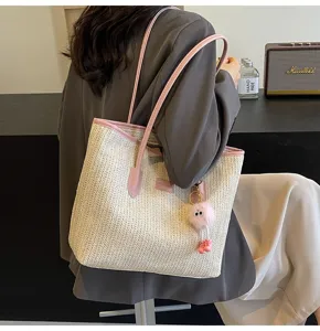 Close-up view of the stylish woven straw tote bag with pink leather handles and cute charm detail.