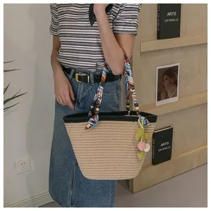 Detailed shot of the woven straw tote bag with silk scarf handle and cute pom-pom pendant.