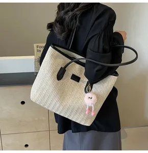 Close-up detail of straw woven tote bag with black leather trim and cute furry pink charm.