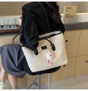 Large capacity straw woven tote bag with contrast black trim and cute pink doll pendant.