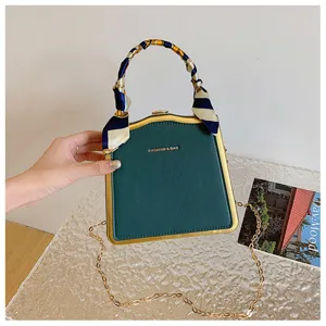 Sac de soirée structuré vert avec cadre doré, bandoulière chaîne et foulard en soie.